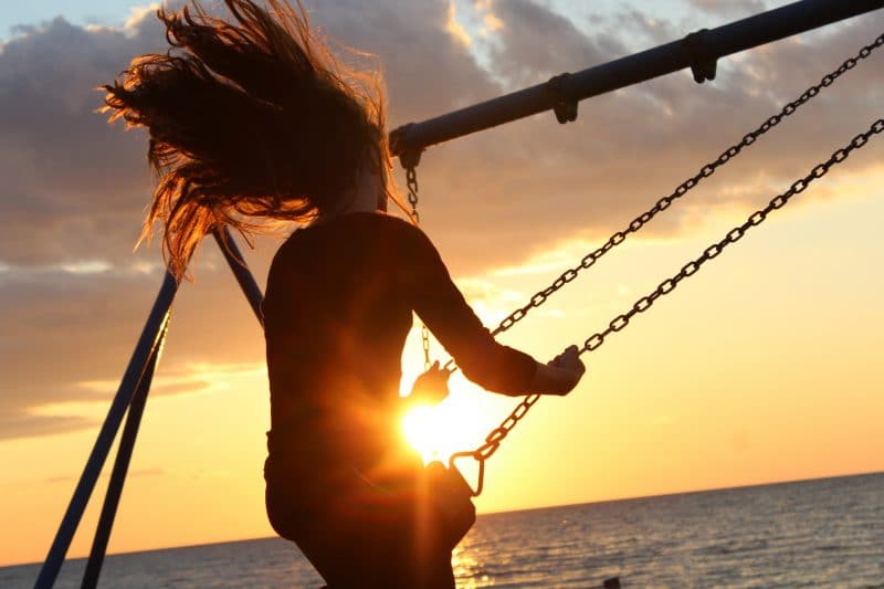 Women on a swing in front of ocean, having fun.